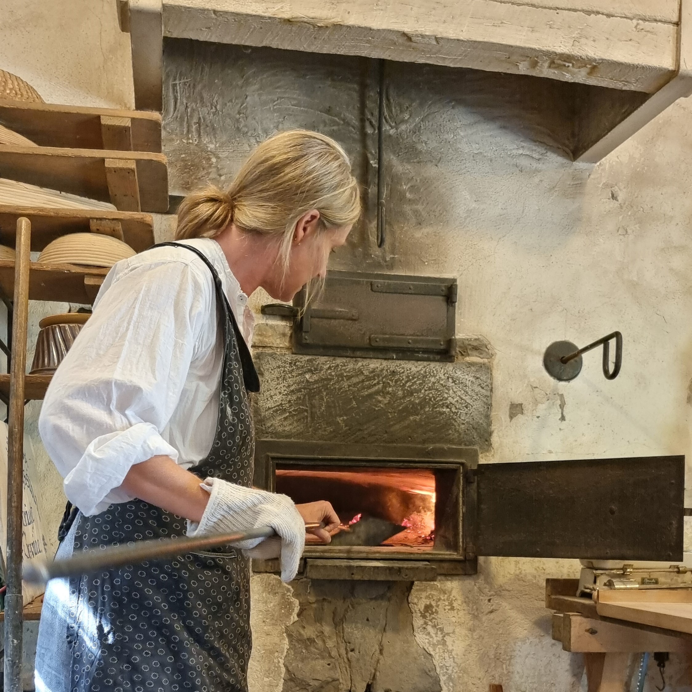 Backen im Backhaus, historische Hausfrau schiebt ein Brot in den Ofen