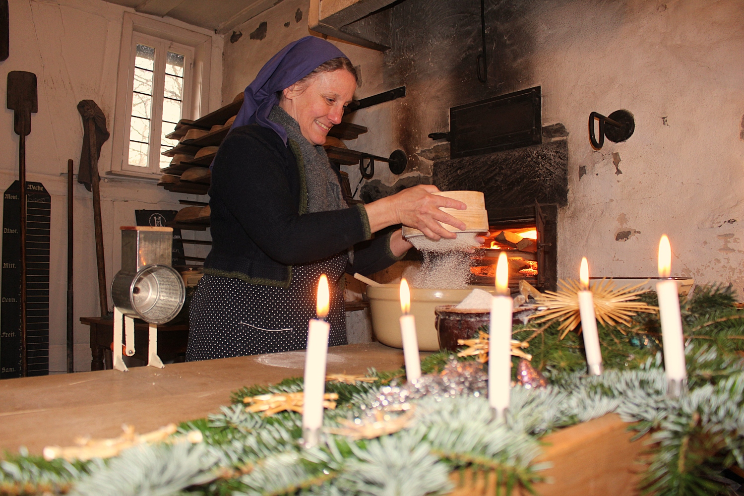 Historische Hausfrau im Backhaus zur Weihnachtszeit mit brennenden Kerzen
