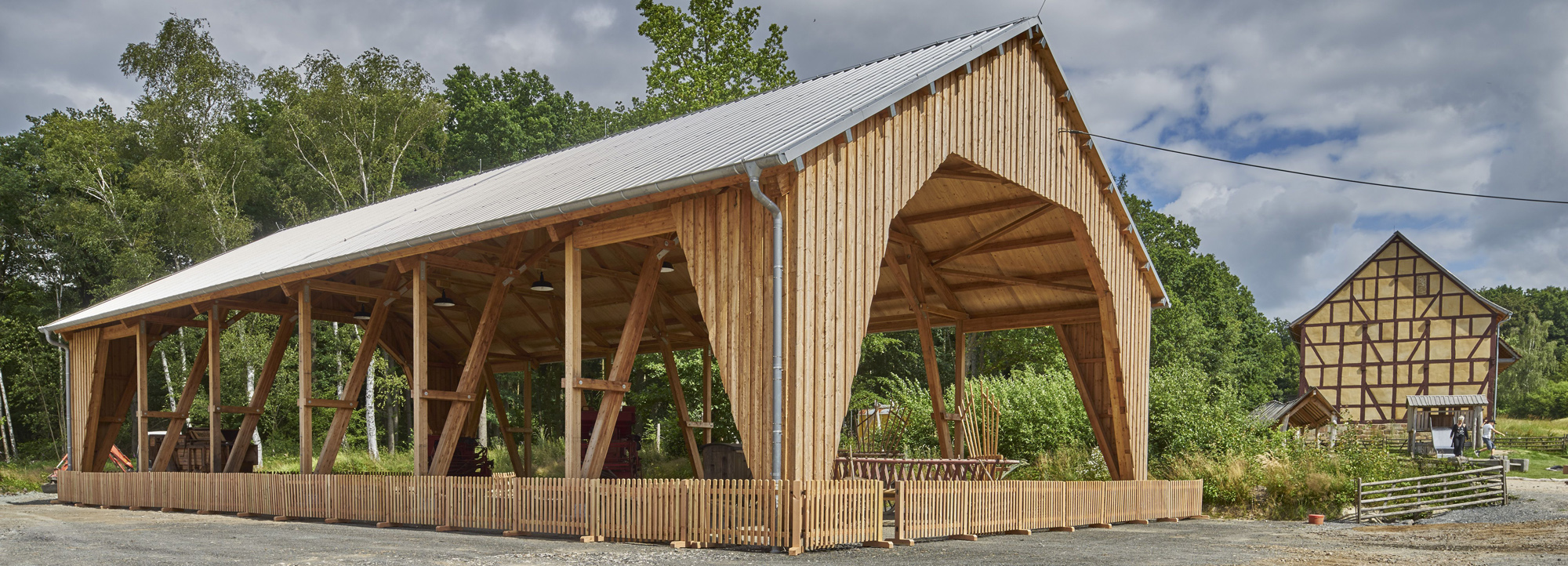 Außenansicht der Dreschhalle, offene Schneunenkonstruktion aus Holz auf geschottertem Platz.