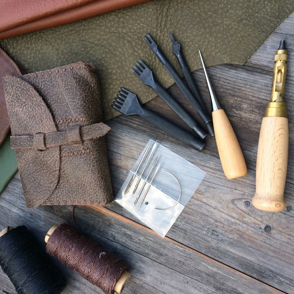 Verschiedene Utensilien zur Lederverarbeitung auf einem Holztisch.