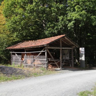 Feldbrandziegelei am Wegesrand einer geschotterten Straße. Dahinter stehen verschiedene Laubbäume.