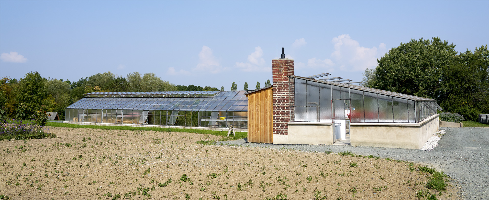 Ein Gewächshaus in L-Form mit der kurzen Front im Vordergrund. Davor ein unbepflanzter Acker.