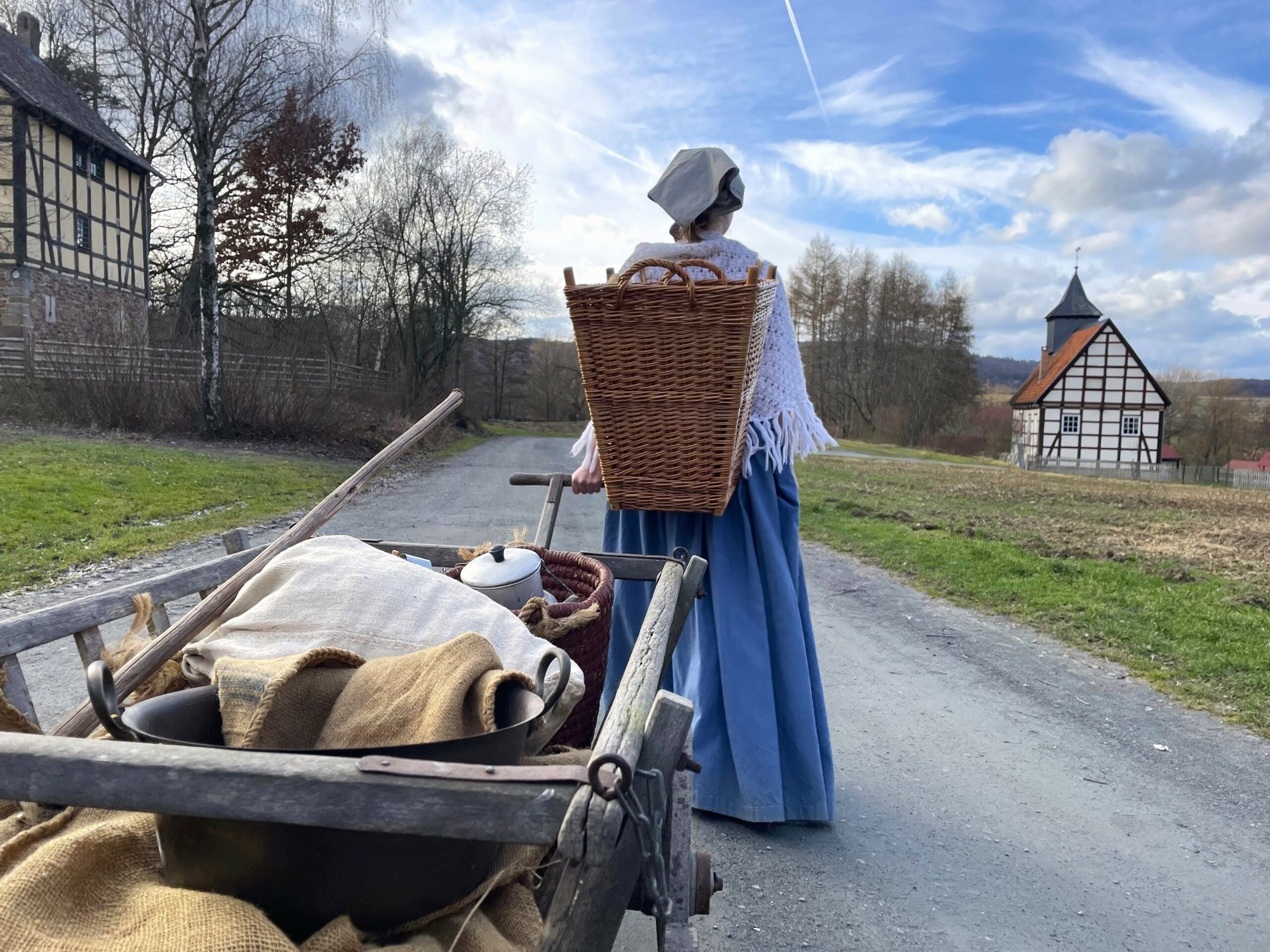 Frau im historischen Kostüm, voll bepackt mit Kiepe und Handwagen.