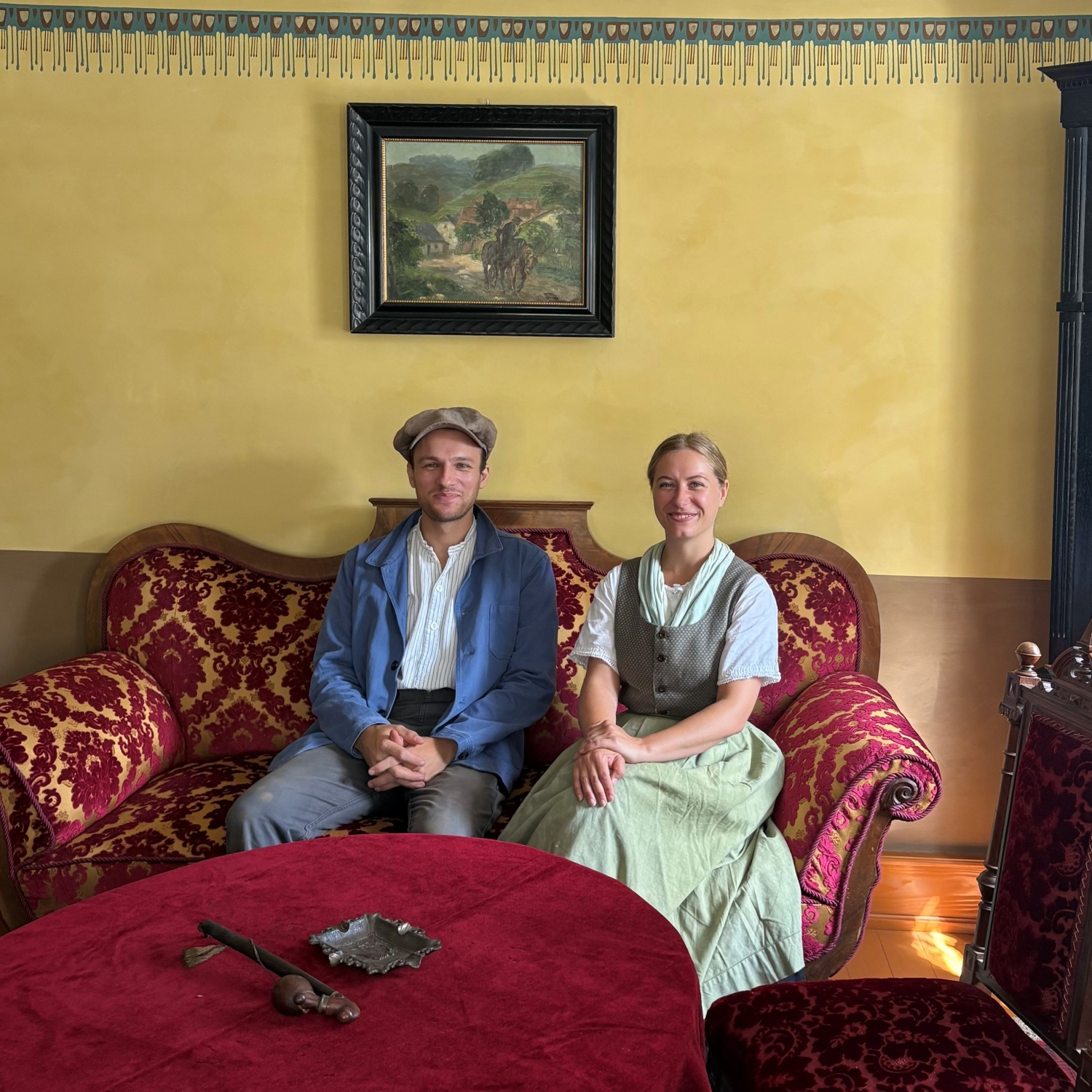 Das Jungbauernpaar sitzt auf einem roten Sofa im Haus aus Nieder-Gemünden