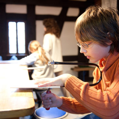 Ein Junge sägt ein Motiv an einem Tisch aus.