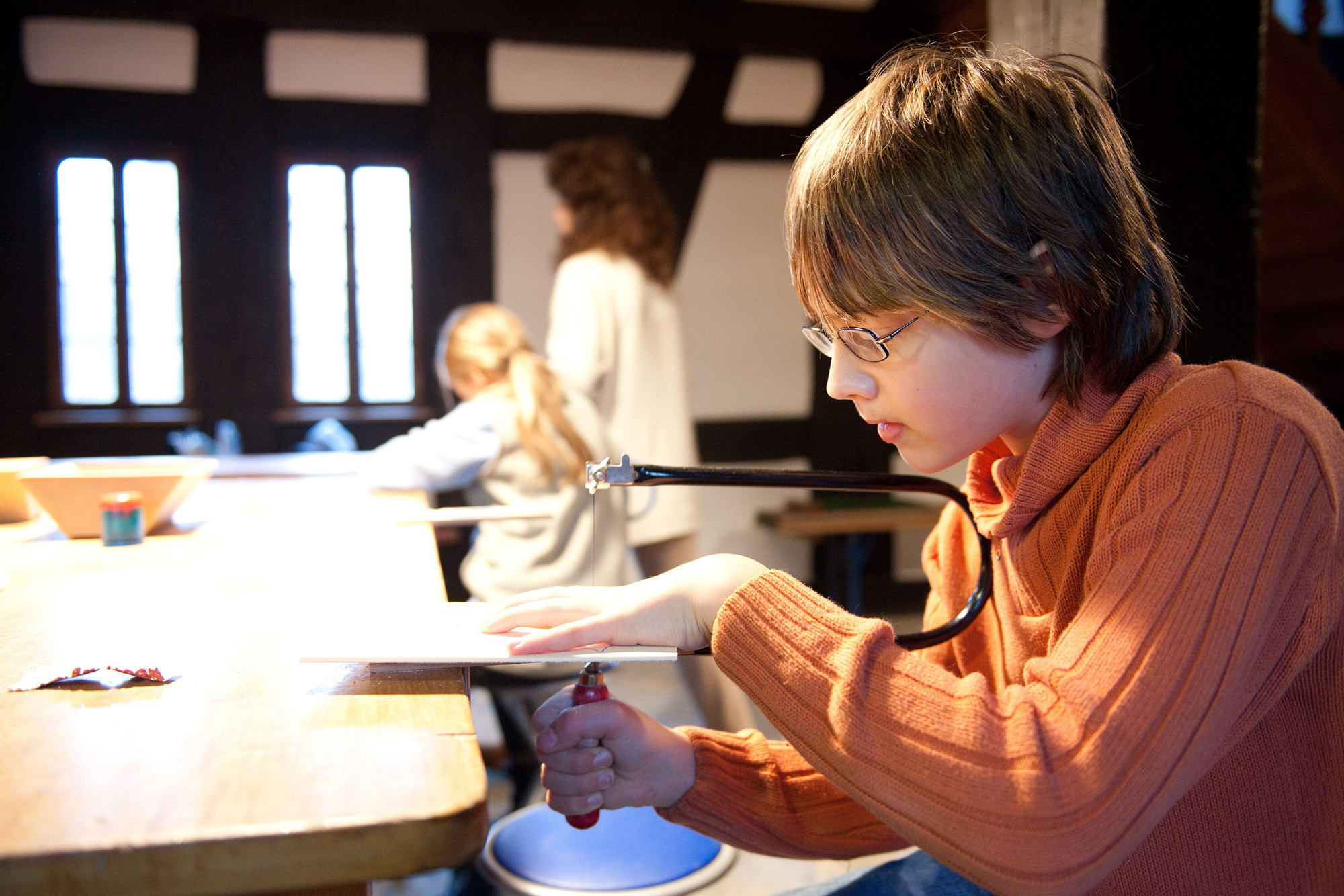 Ein Junge sägt ein Motiv an einem Tisch aus.
