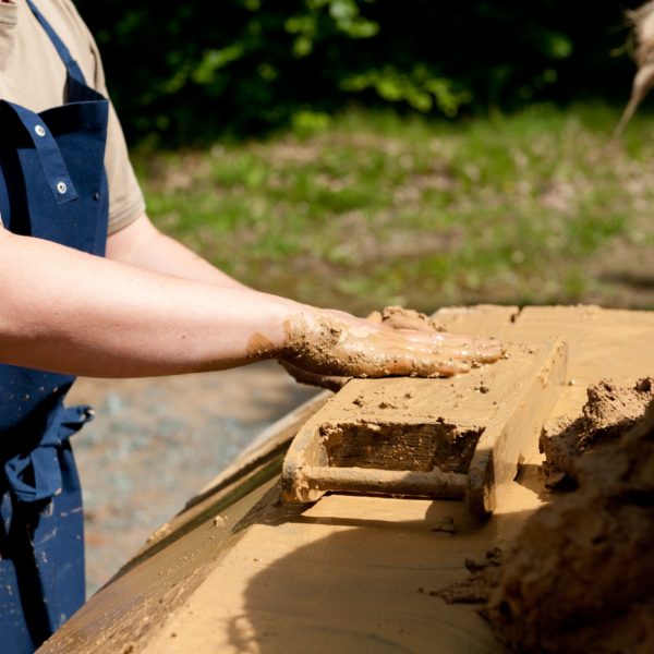 Ein Person streicht den Lehm in der Lehmsteinform mit den Händen glatt.