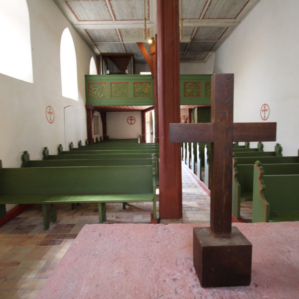 Innenaufnahme der Kapelle aus Lollar: Altar mit Holzkreuz, Blick auf grüne Kirchenbänke.