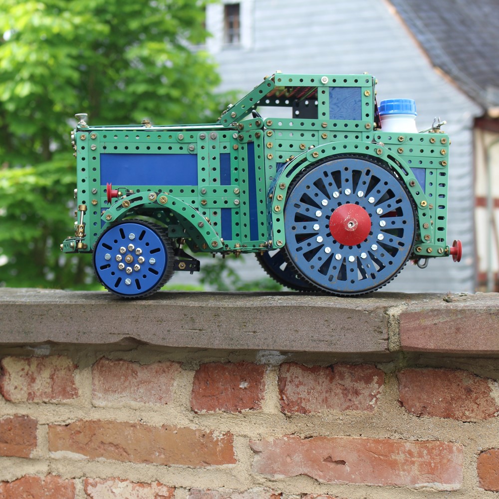 Metallbaukasten-Fahrzeug in grün und blau, steht auf einer Mauer.