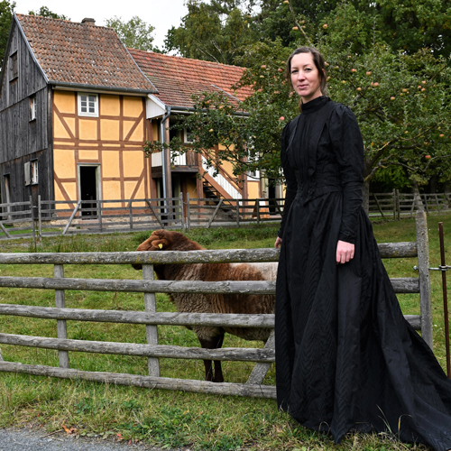 Braut in historischem schwarzen Brautkleid , in Hintergrund ein Schaf und die Synagoge aus Nentershausen.