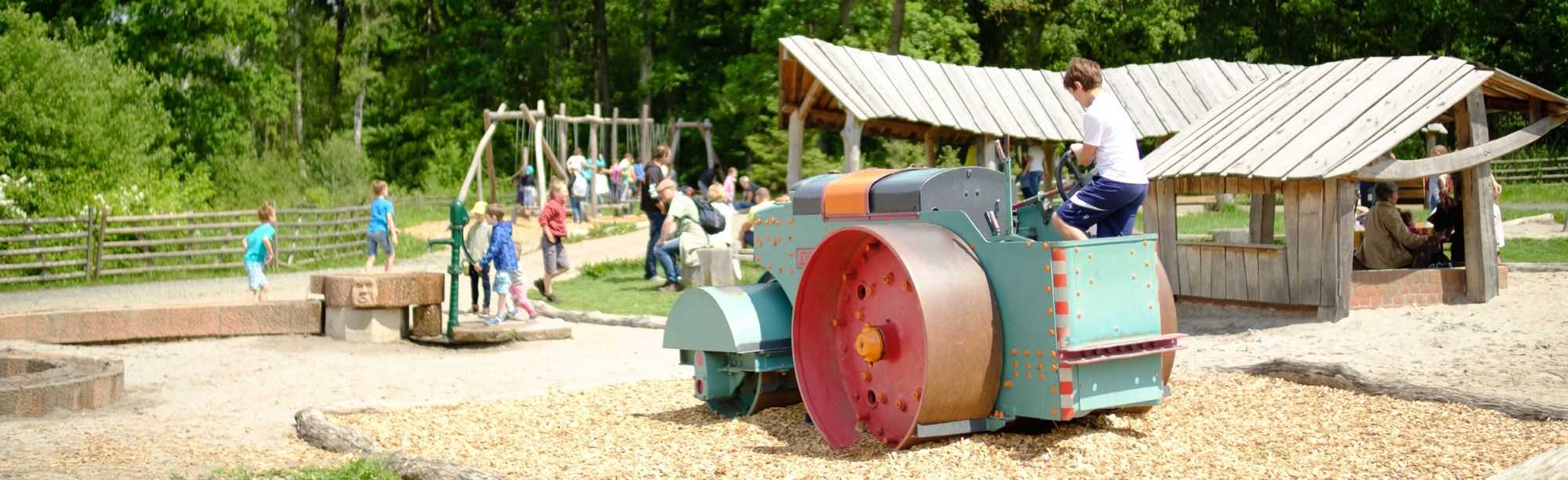 Im Vordergrund steht eine große Metallwalze, auf der Kinder klettern