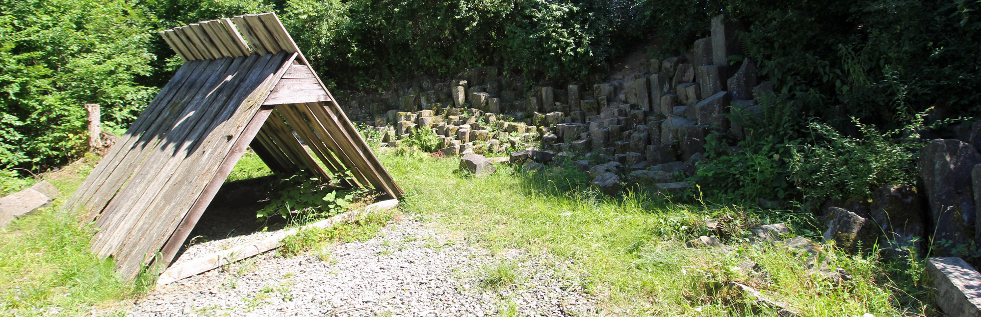 Im Vodergrund eine kleine Zelthütte aus Holz und im Hintergrund der Basaltsteinbruch.