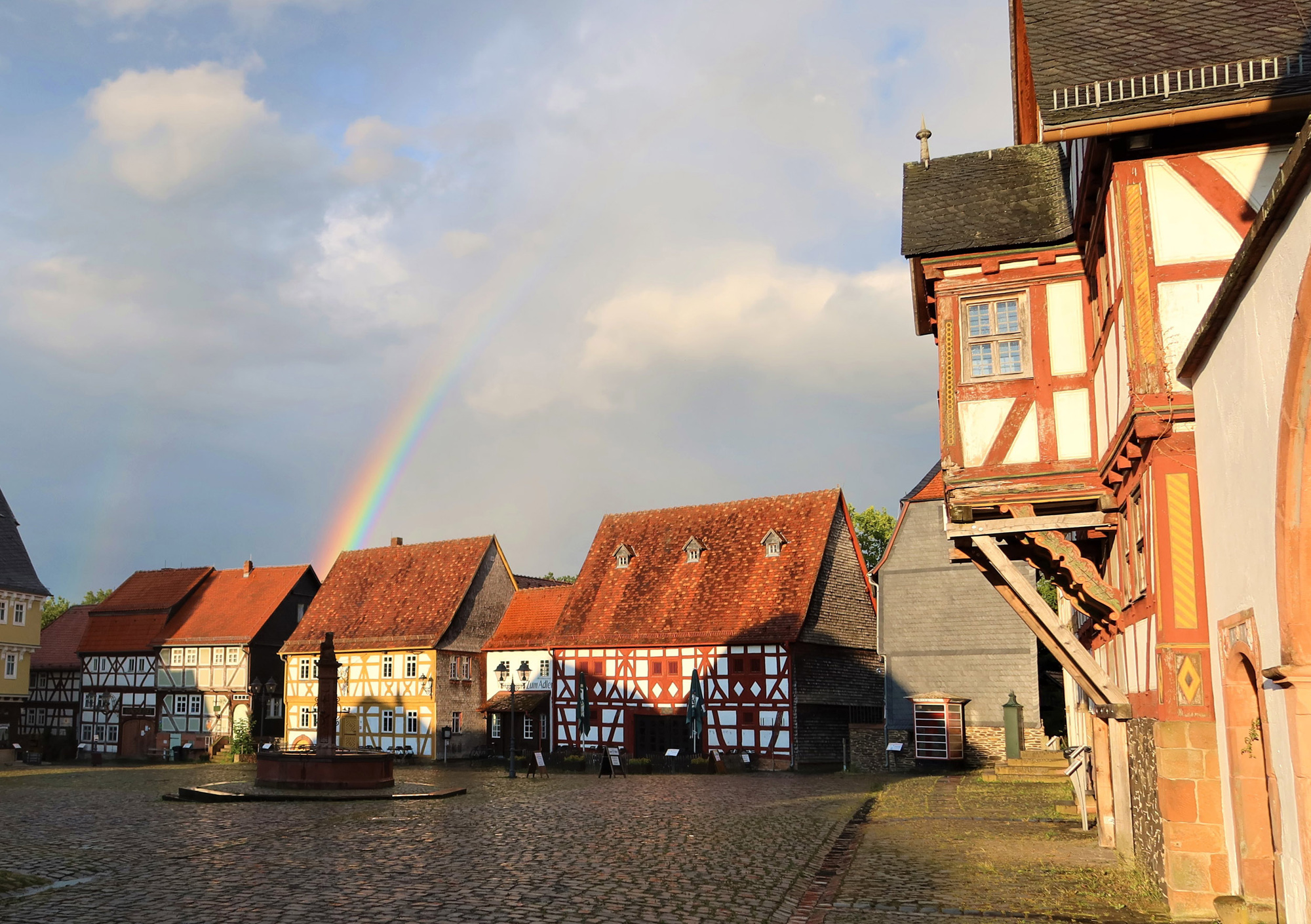 Regenbogen über dem Marktplatz des Freilichtmuseums, man blickt in Richtung des Wirtshauses