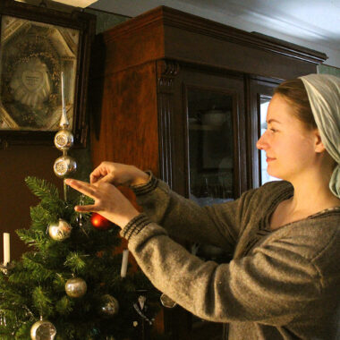 Frau in historischer Kleidung schmückt Weihnachtsbaum mit Glaskugeln