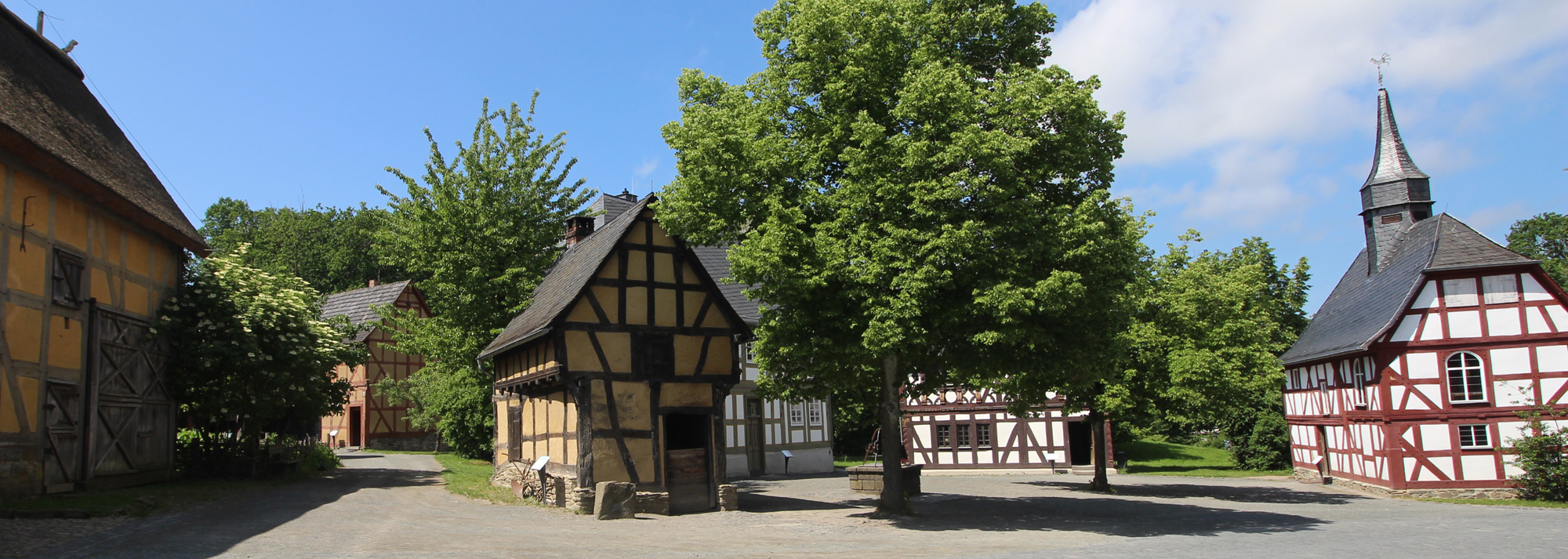 Ein kleines Fachwerkhaus mit dunklen Holzbalken und gelbem Gefache. Es handelt sich um die Schmiede aus Weinbach.